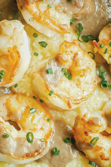 Close-up of creamy shrimp and grits topped with brown gravy and chopped chives, highlighting the texture of the shrimp and the creamy consistency of the grits.