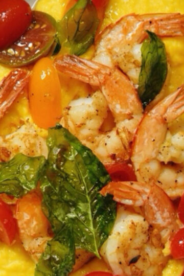 Grilled shrimp served on a bed of creamy yellow polenta, topped with cherry tomato halves and crispy basil leaves.