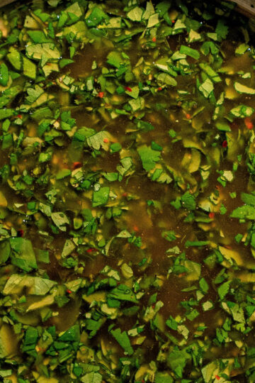 A close-up of a bowl filled with chimichurri sauce, showing finely chopped green herbs mixed with oil and vinegar.
