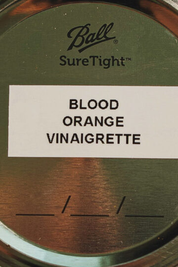 A metal jar lid with a white label that reads “BLOOD ORANGE VINAIGRETTE.” The lid has the “Ball Sure Tight” logo printed above the label.