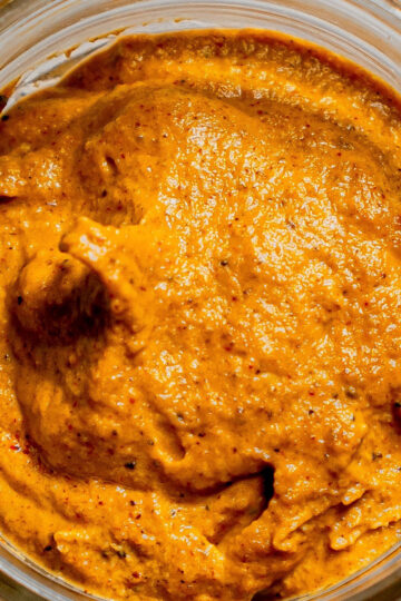 Close-up view of a glass jar filled with a thick, orange-brown paste or sauce with a smooth, slightly textured surface.