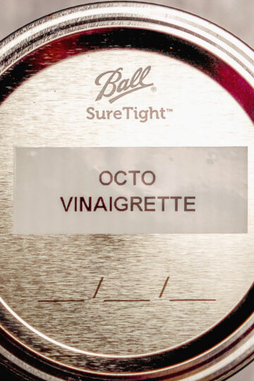 A close-up of a Ball SureTight metal jar lid labeled OCTO VINAIGRETTE with blank lines underneath the label.