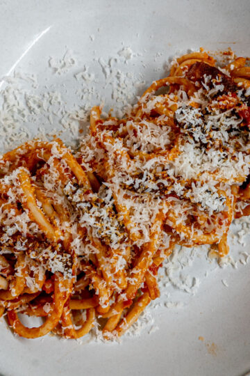 A plate of spaghetti topped with tomato sauce and grated cheese, arranged neatly on a white dish.