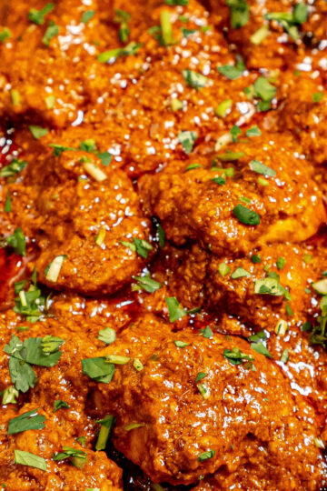 A close-up of a spicy curry dish with chunks of meat in a rich, reddish-brown sauce, garnished with chopped fresh cilantro.