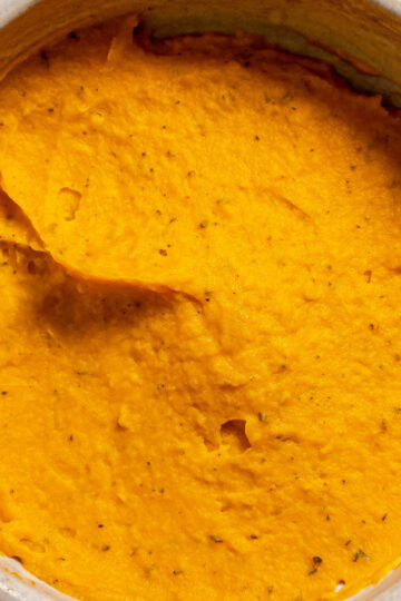 A bowl filled with smooth, bright orange mashed sweet potatoes, with a creamy texture and specks of seasoning visible throughout.