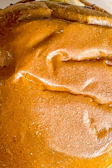 Close-up of a golden-brown, slightly wrinkled bread roll or bun with a shiny surface and some darker, toasted areas on top.