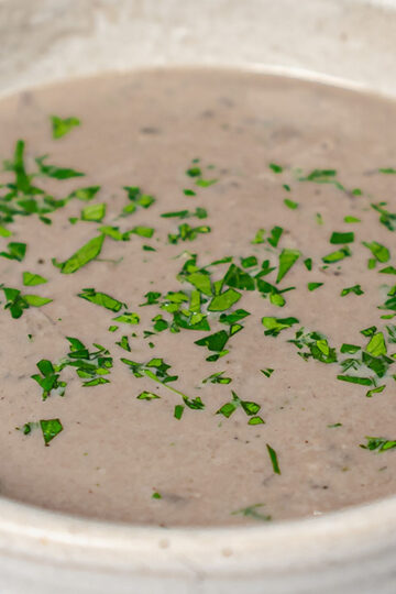 A bowl of creamy mushroom soup garnished with freshly chopped parsley.