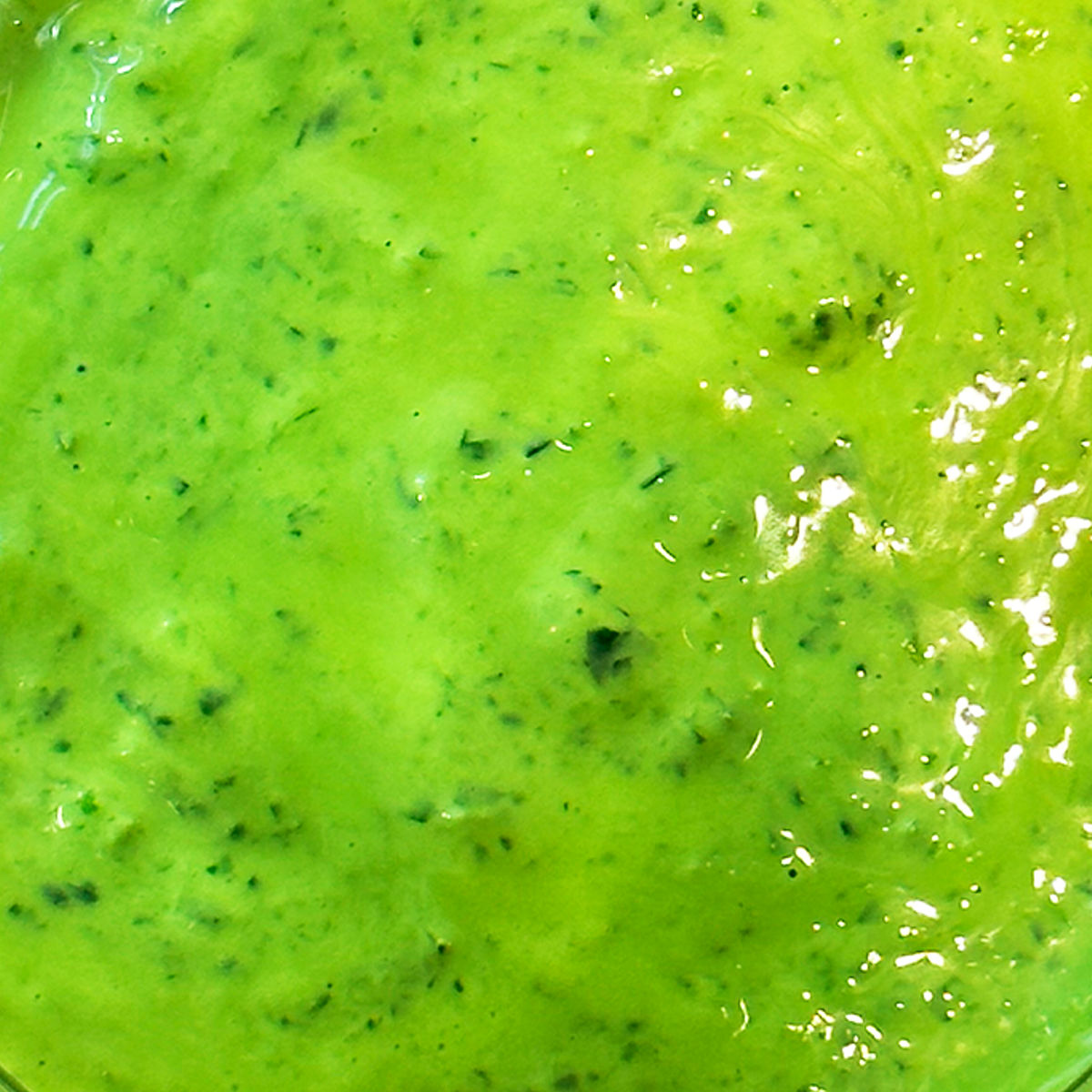 Bright green, creamy sauce with a slightly chunky texture and visible flecks of herbs, glistening under the light.