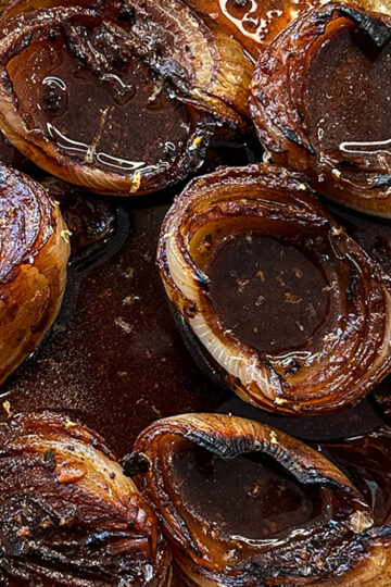 Close-up of caramelized onion halves in a dark, glossy sauce, seasoned with pepper and salt, arranged closely together on a plate.