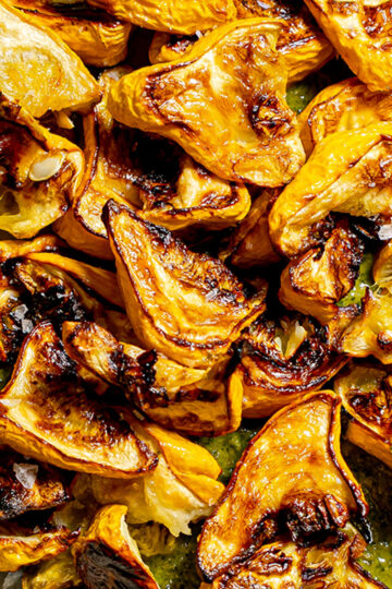 Close-up of roasted golden-yellow squash pieces with charred edges, served on a green sauce, with a sprinkling of coarse salt visible on top.
