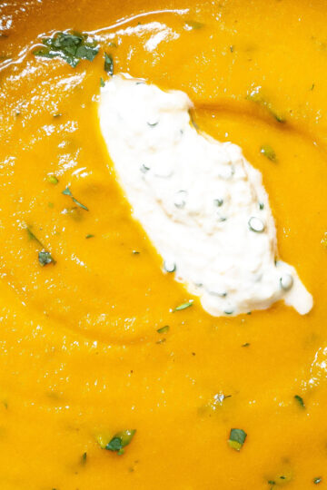 A close-up of creamy orange soup garnished with a dollop of herbed cream and sprinkled with chopped fresh herbs.