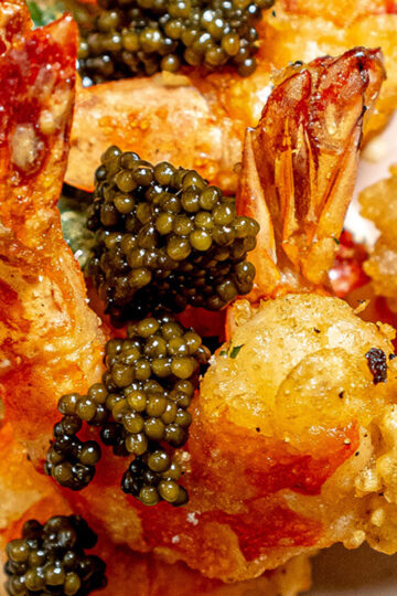 Close-up of crispy fried shrimp topped with generous spoonfuls of glistening black caviar, showcasing a rich, golden texture and luxurious garnishing.
