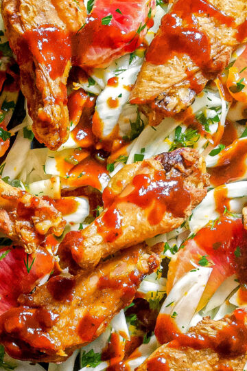 Barbecue-glazed chicken wings served on a bed of thinly sliced fennel, fresh herbs, and bright grapefruit segments. The dish is colorful with rich red sauce contrasting the pale fennel and vibrant citrus.