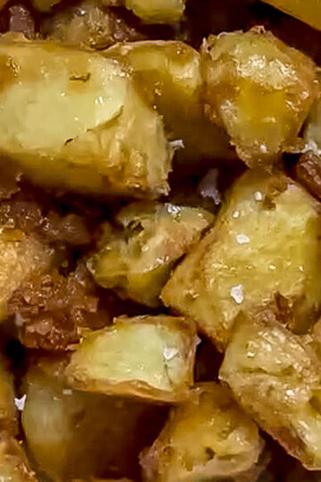 Close-up of crispy, golden-brown roasted potato cubes with visible flakes of salt and slightly caramelized edges.