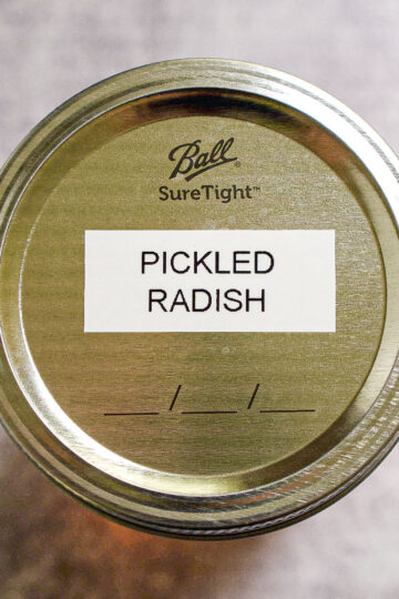 A metal canning jar lid labeled PICKLED RADISH with the Ball SureTight logo, viewed from above against a gray background.