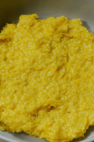 A bowl of finely mashed yellow yam, forming a smooth, thick, and slightly textured paste, served in a light-colored dish.