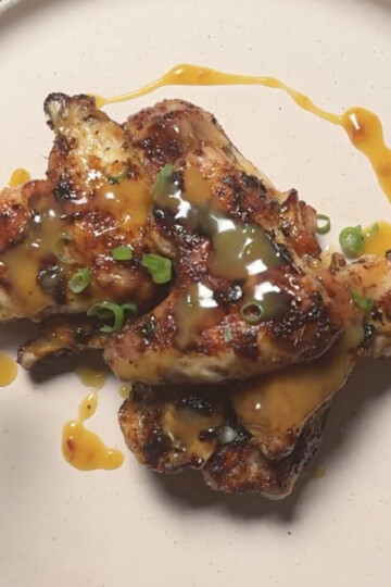 Grilled chicken wings topped with chopped green onions and drizzled with a golden-brown sauce, served on a plain white plate.