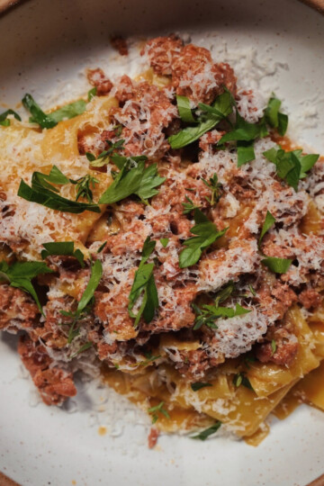 A bowl of pasta topped with a meat sauce, grated cheese, and fresh parsley, served on a white ceramic plate.