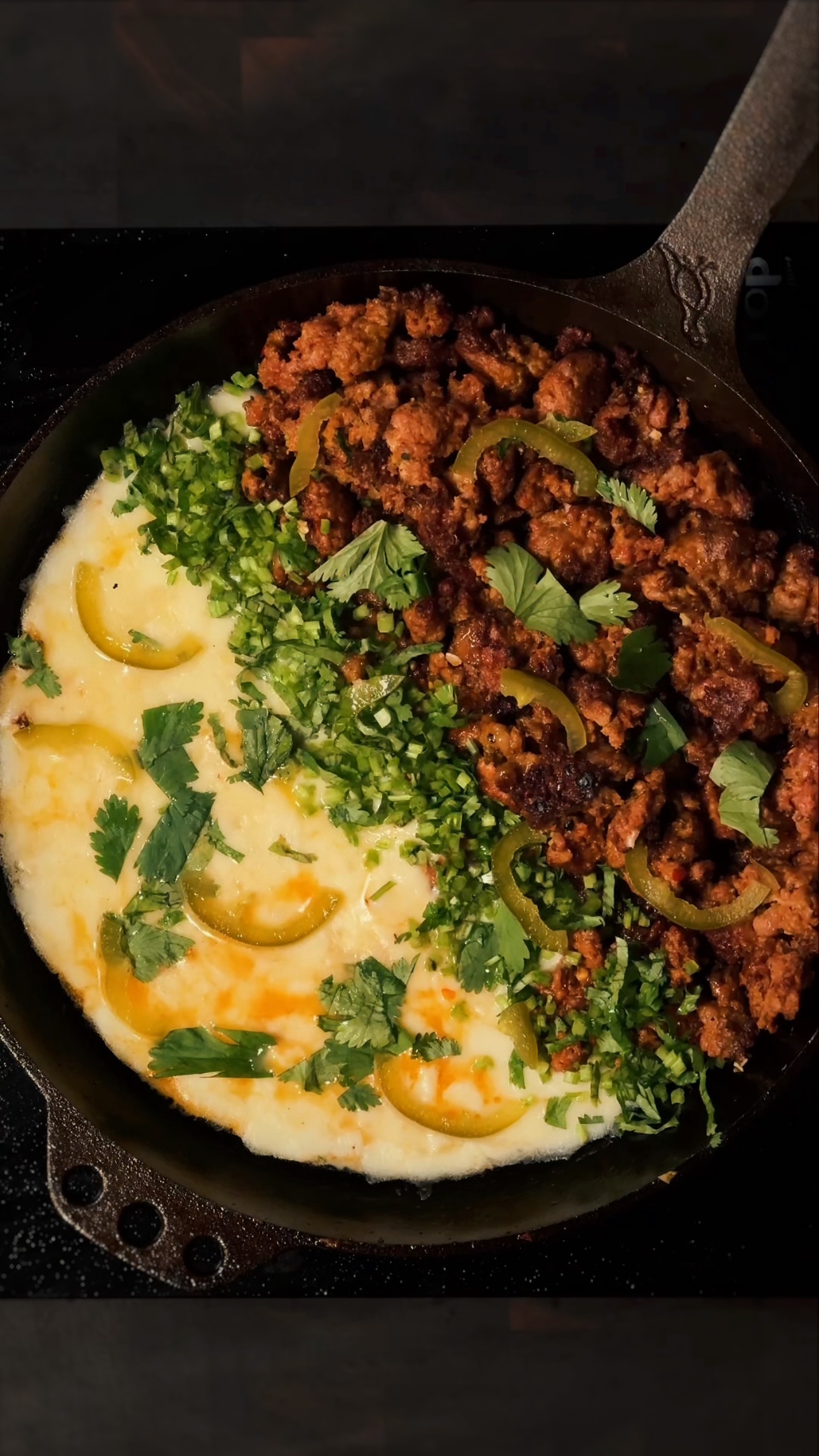 A skillet filled with melted cheese topped with cooked ground meat, sliced yellow peppers, and chopped fresh cilantro and green onions, creating a colorful and appetizing dish.