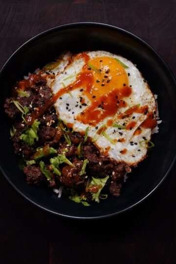 Asian beef rice bowl with glazed ground beef, fried egg, green onions, and sesame seeds