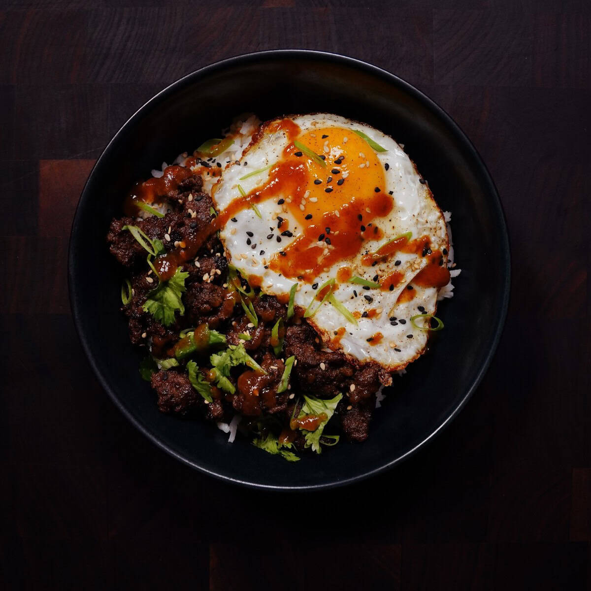 Asian beef rice bowl with glazed ground beef, fried egg, green onions, and sesame seeds