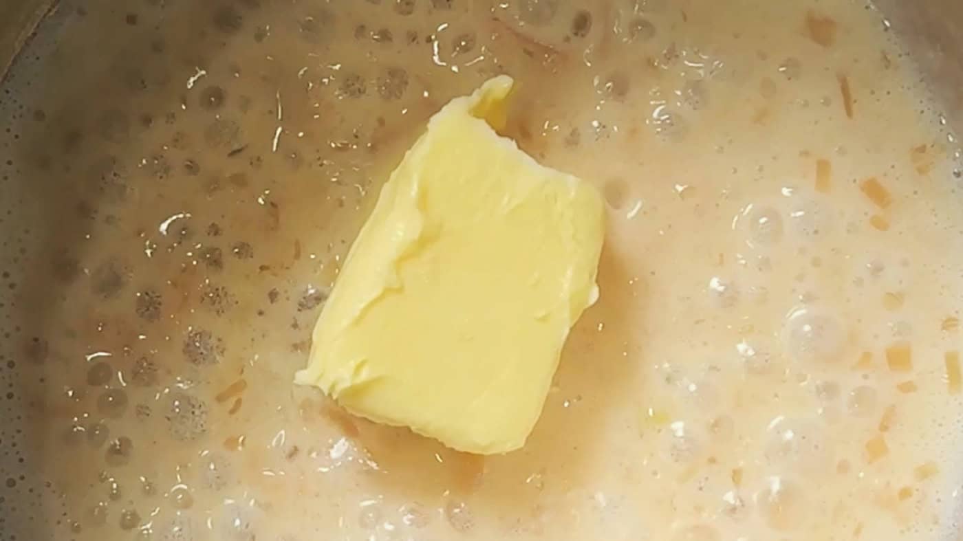 A slab of cold butter sitting on a warm shallot and wine reduction in a pan.