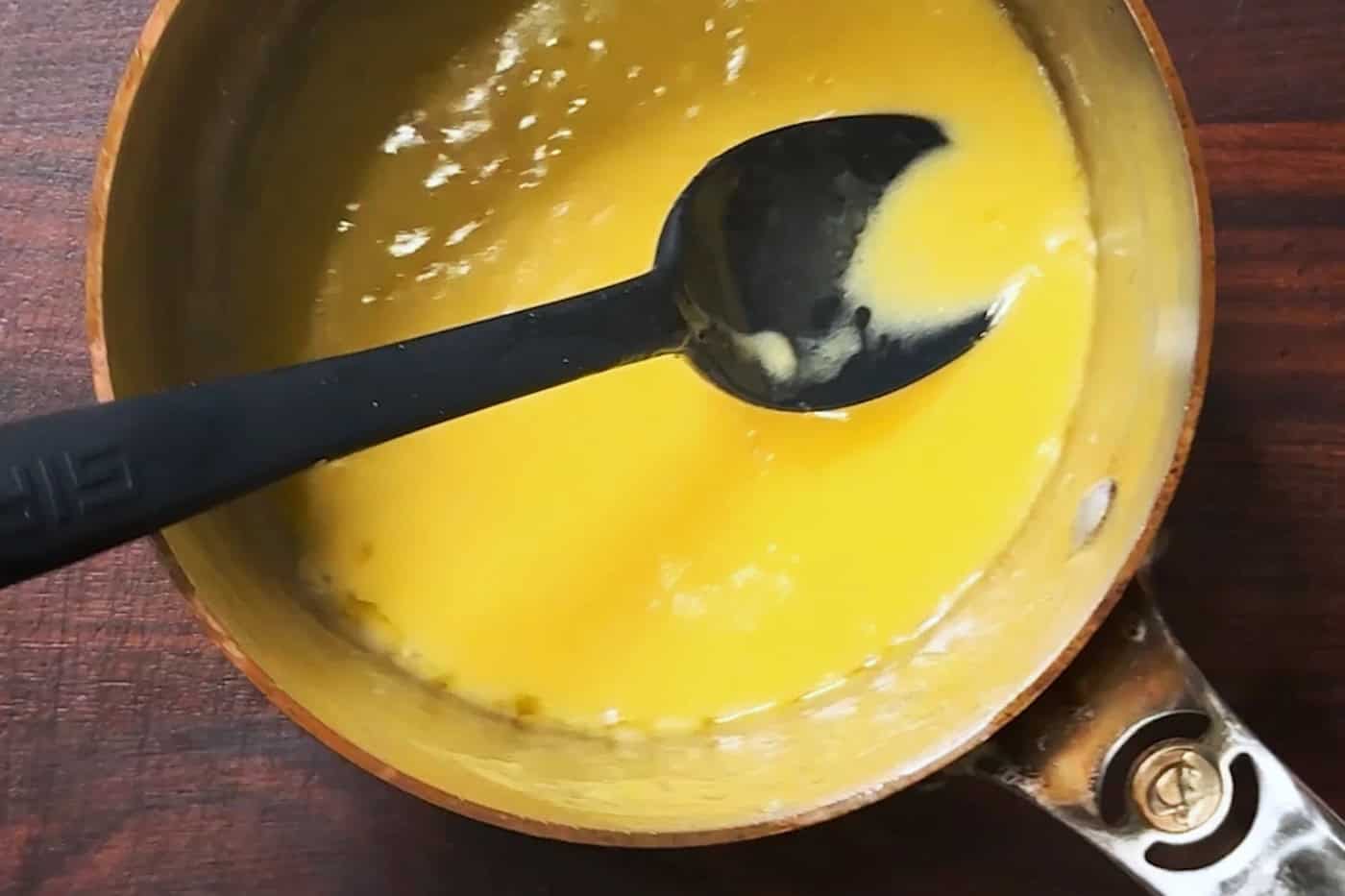 A small copper pan of finished beurre blanc on a wooden board, with a spoon resting in it.