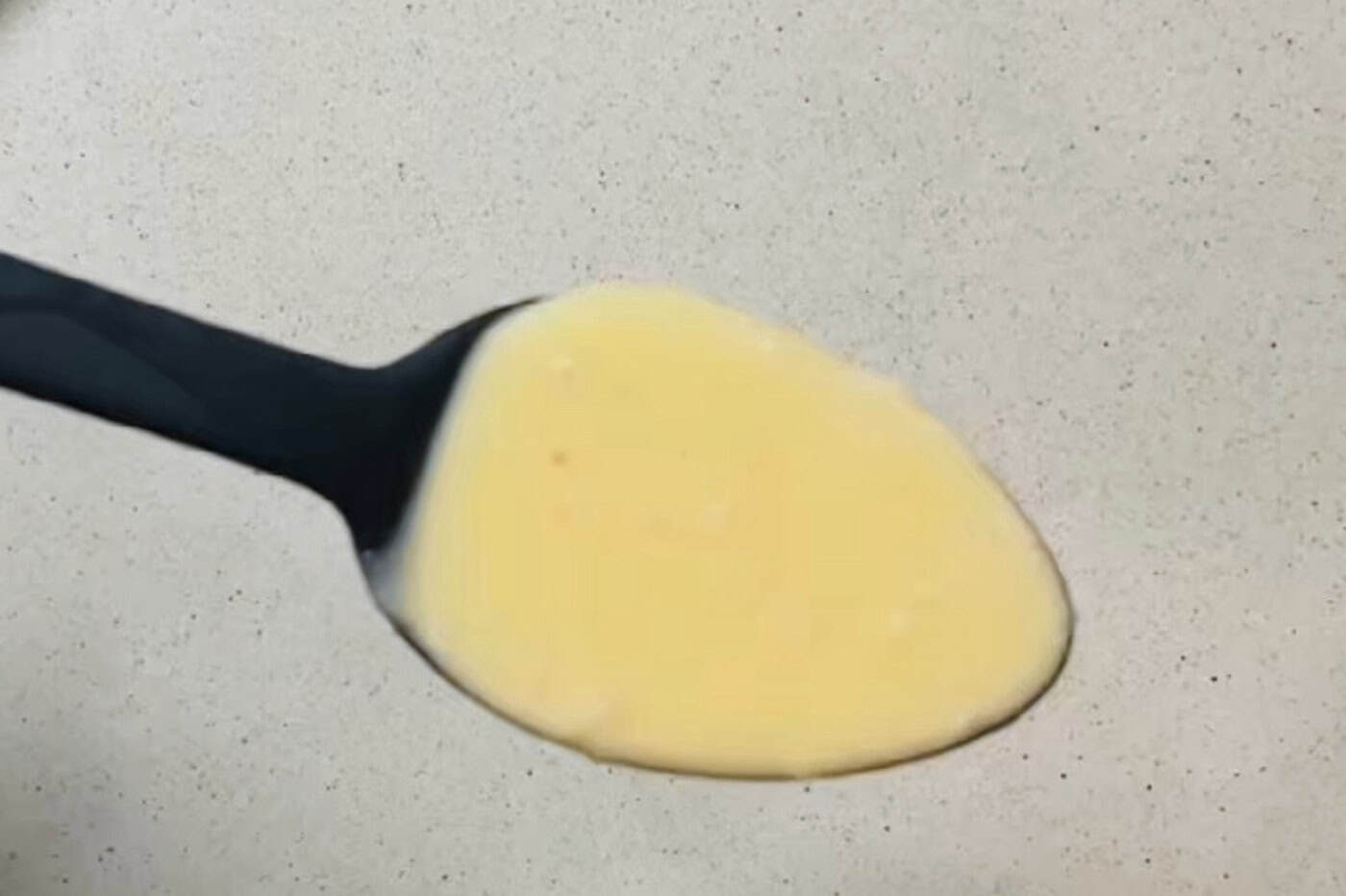A spoonful of beurre blanc held over a pale ceramic plate, thick enough to coat the spoon.