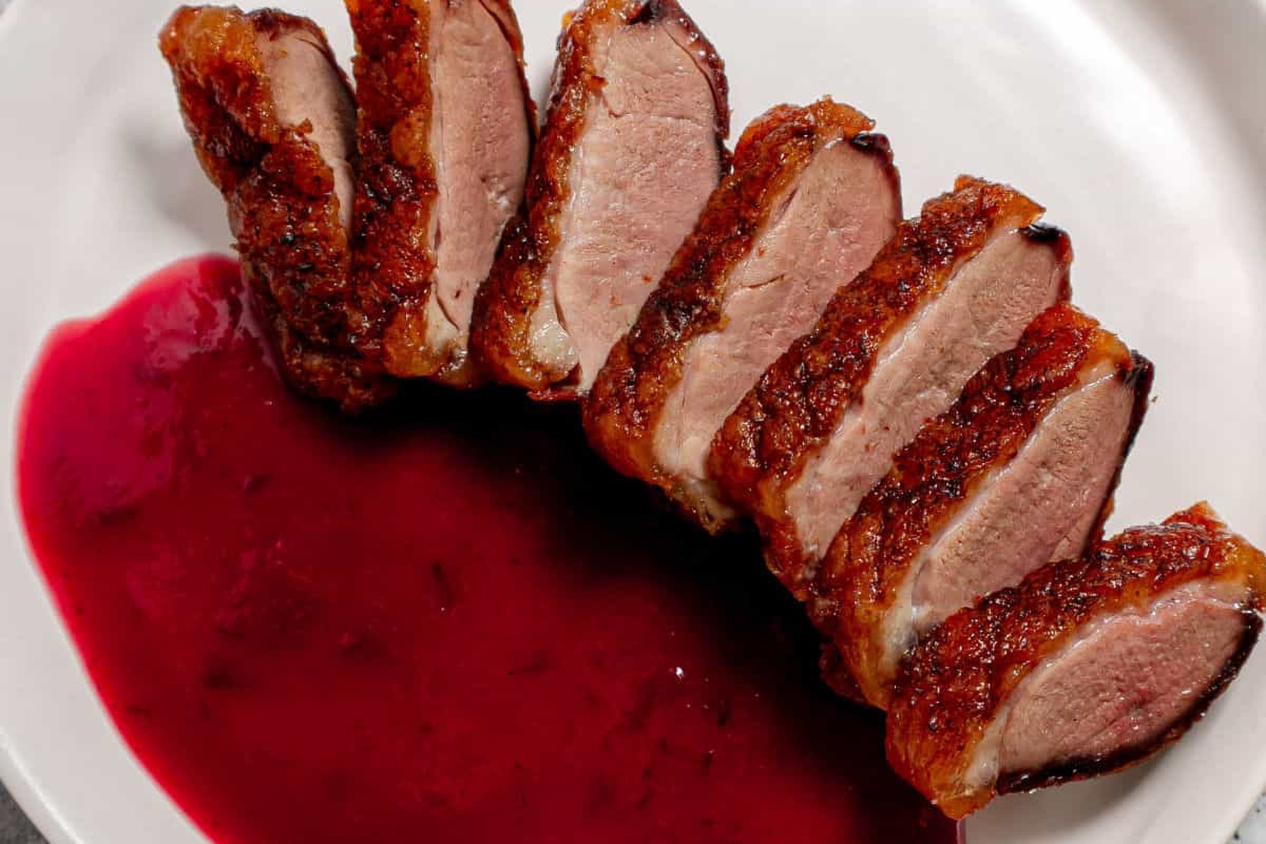 Sliced duck breast beside a deep red plum sauce reduced until it coats the plate.