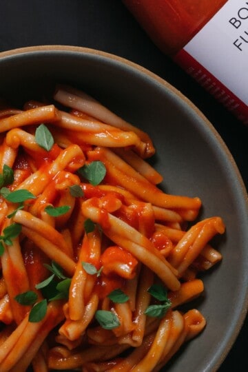 A bowl of casarecce in tomato sauce beside a bottle of Bona Furtuna passata.