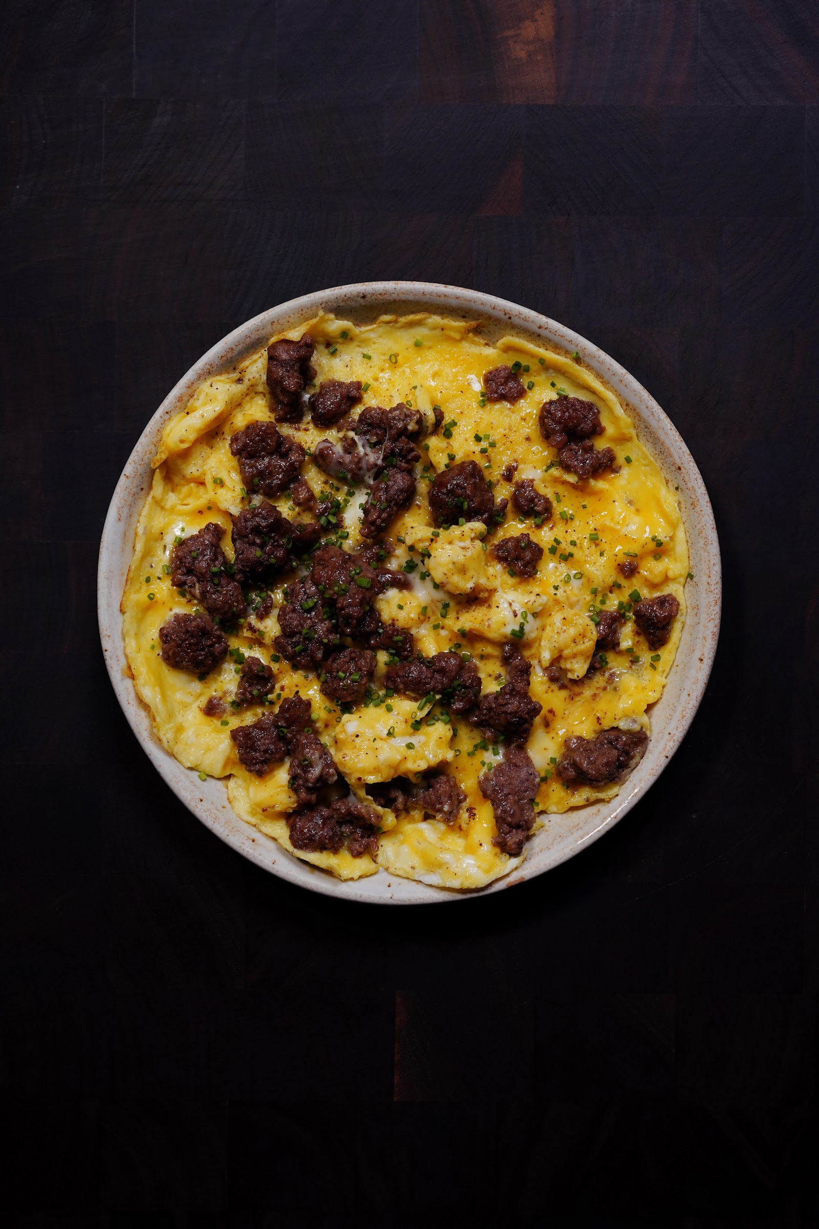 Soft scrambled eggs with crispy browned ground beef and chives on a ceramic plate